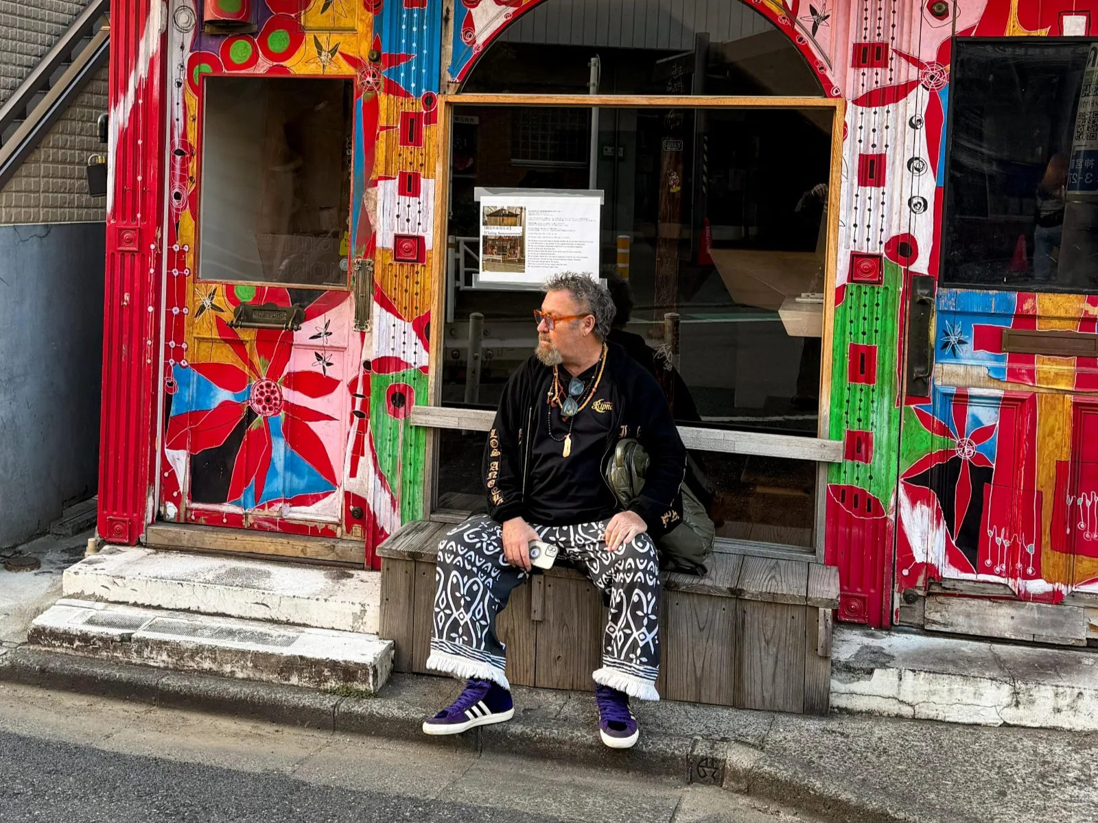 Stephen Lasker seated on a bench outside a painted shopfront